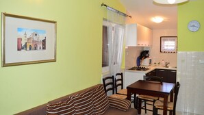 A compact living space with a sofa, dining table, chairs, a kitchen area with a stove, and a clock on the wall. - Apartments Branko / Joanna / Two Bedrooms (Tribunj)