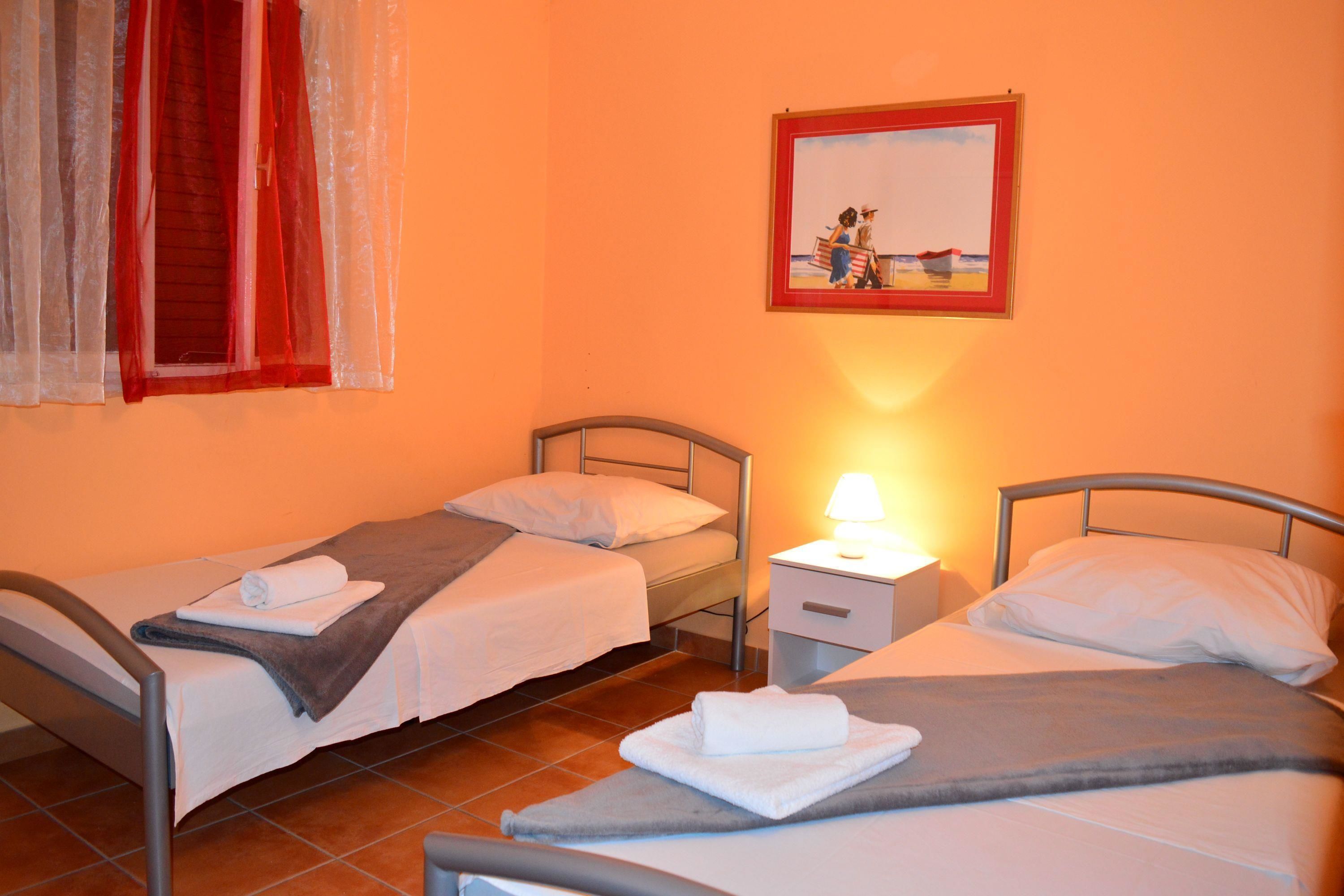 A room with two single beds, a nightstand with a lamp, and a painting on the wall.