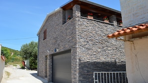 A two-story stone building with a garage door, a balcony with potted plants, and a clear sky. - Apartments Branko / Joanna / Two Bedrooms (Tribunj)