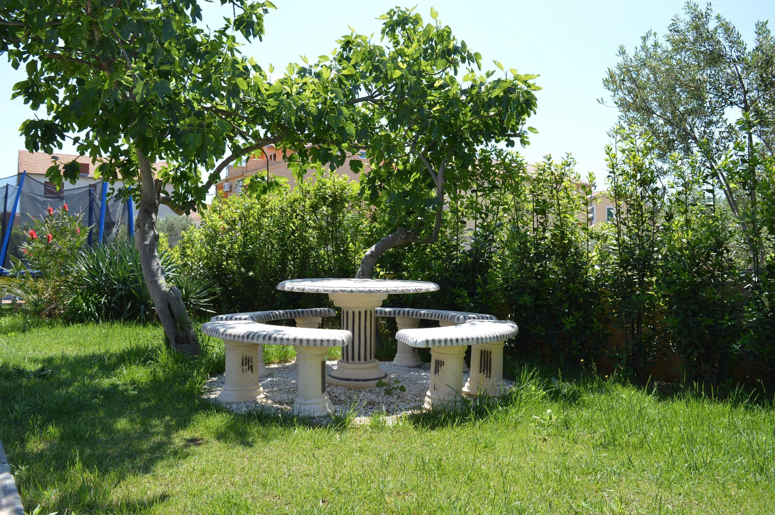 Un jardin avec une table ronde et quatre chaises, entouré de pelouse et d’arbres.