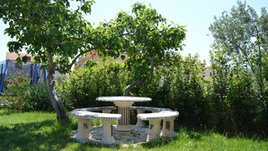 A garden with a round table and four chairs, surrounded by grass and trees. - Apartments Branko / Joanna / Two Bedrooms (Tribunj)