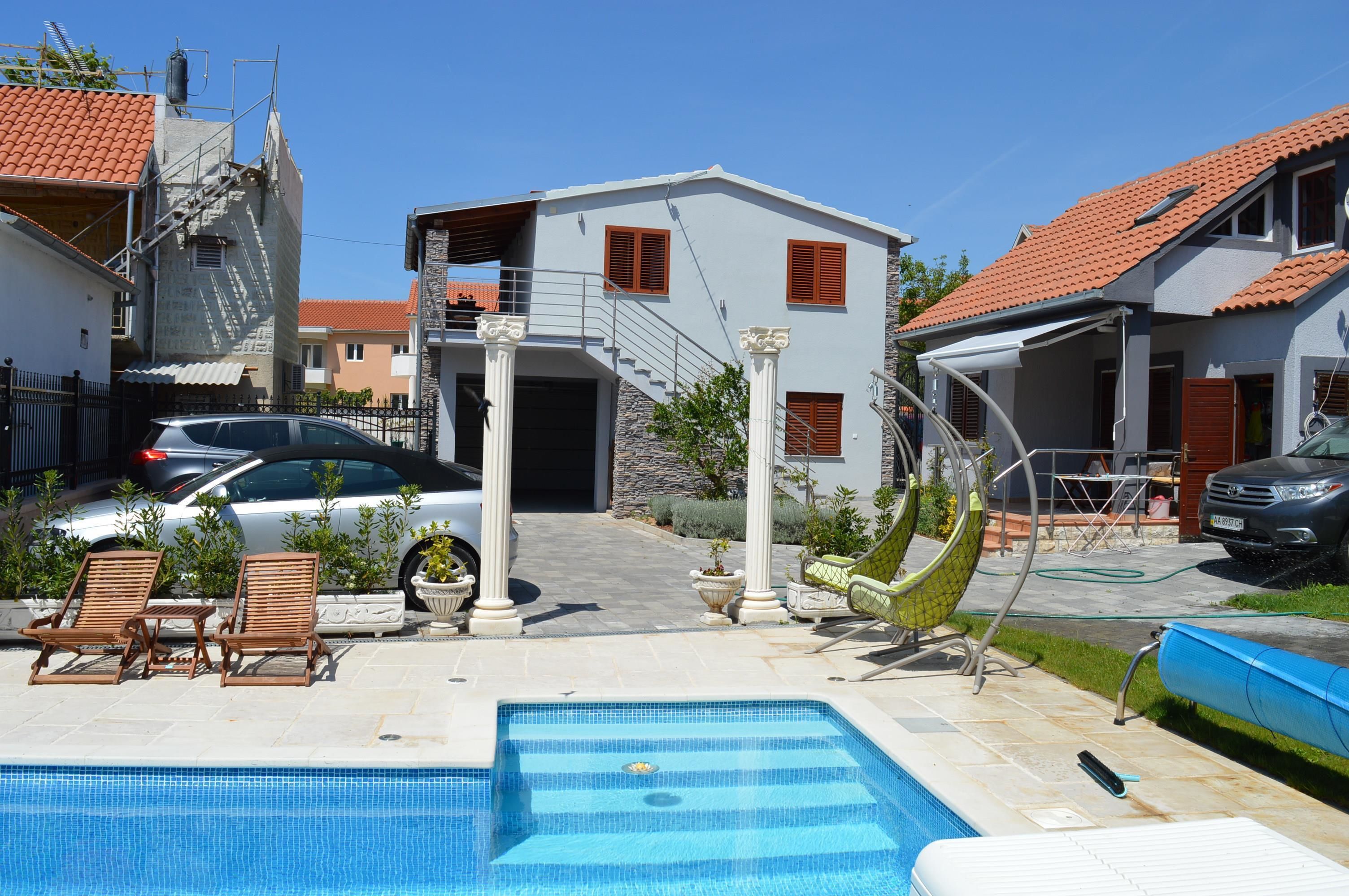 Il s’agit d’une propriété résidentielle dotée d’une piscine, avec une voiture garée devant et un escalier menant à l’entrée.