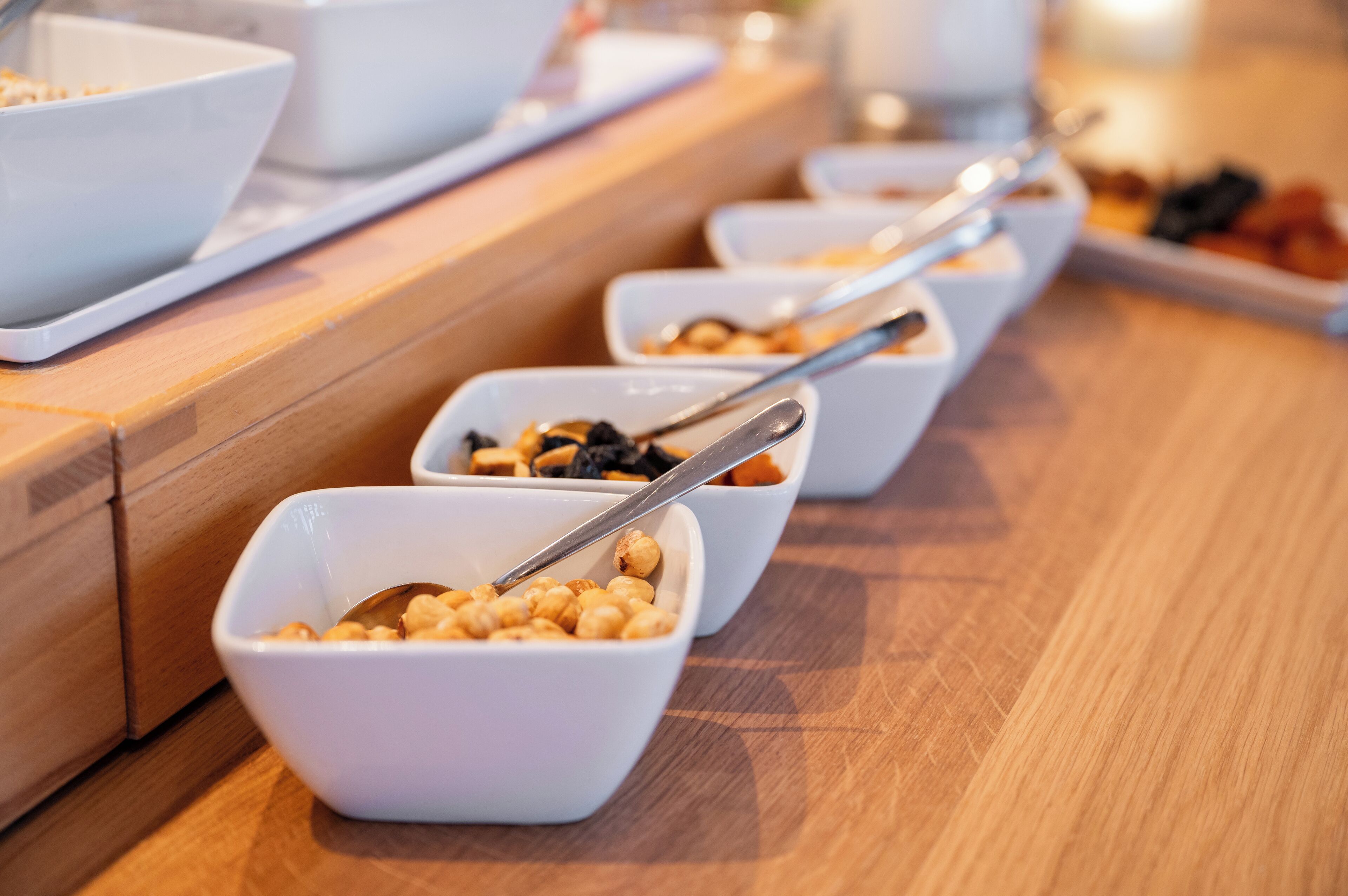 Een buffet met verschillende soorten eten in witte kommen, gerangschikt op een houten toonbank.