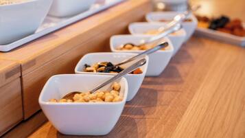 Een buffet met verschillende soorten eten in witte kommen, gerangschikt op een houten toonbank.