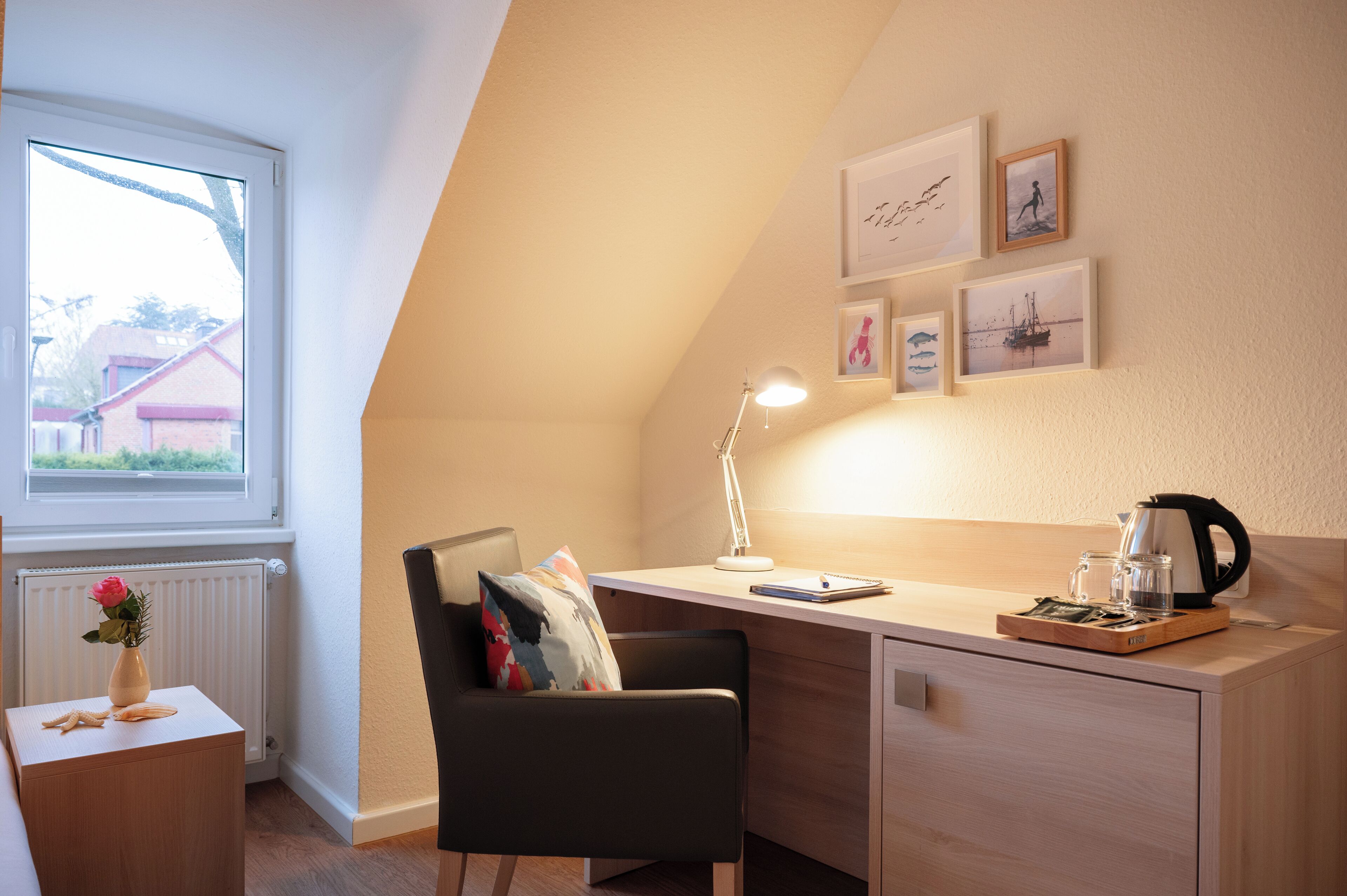 A modern, well-lit room with a desk, chair, and a window overlooking a residential area.