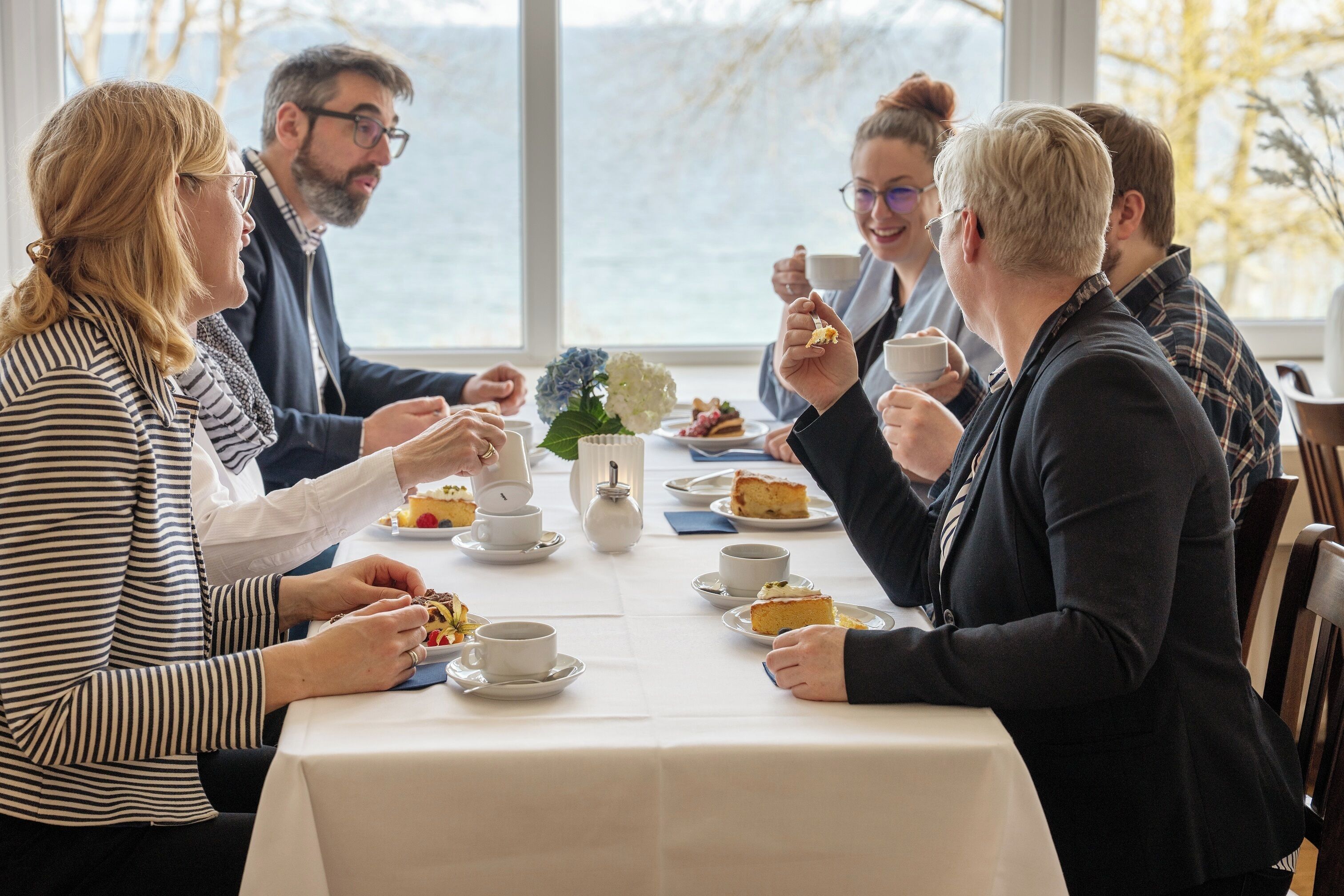 Eine Gruppe von Personen sitzt an einem Tisch und genießt eine Mahlzeit mit Blick auf das Meer.