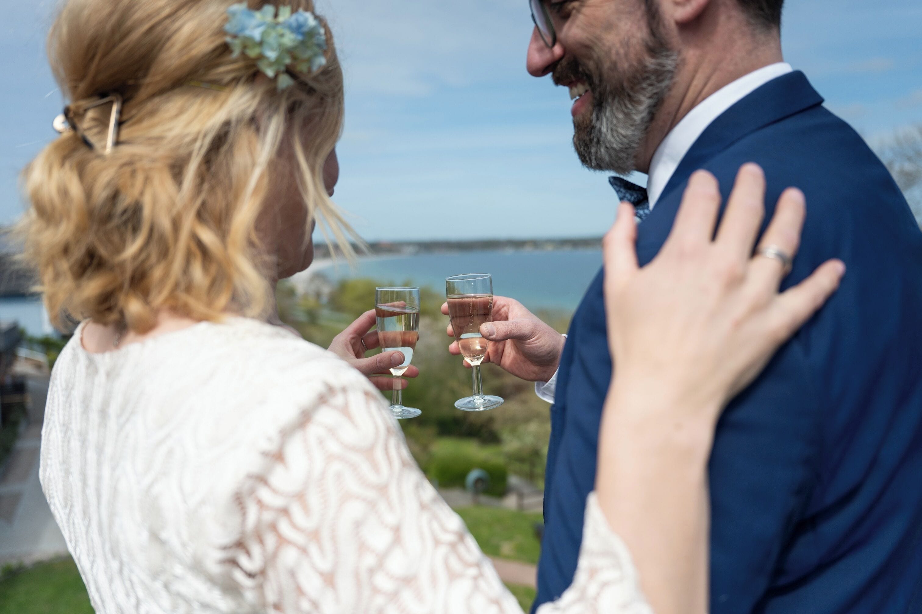 A couple toasting with wine glasses, a scenic outdoor view, and a body of water in the background.