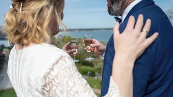 A couple toasting with wine glasses, a scenic outdoor view, and a body of water in the background.
