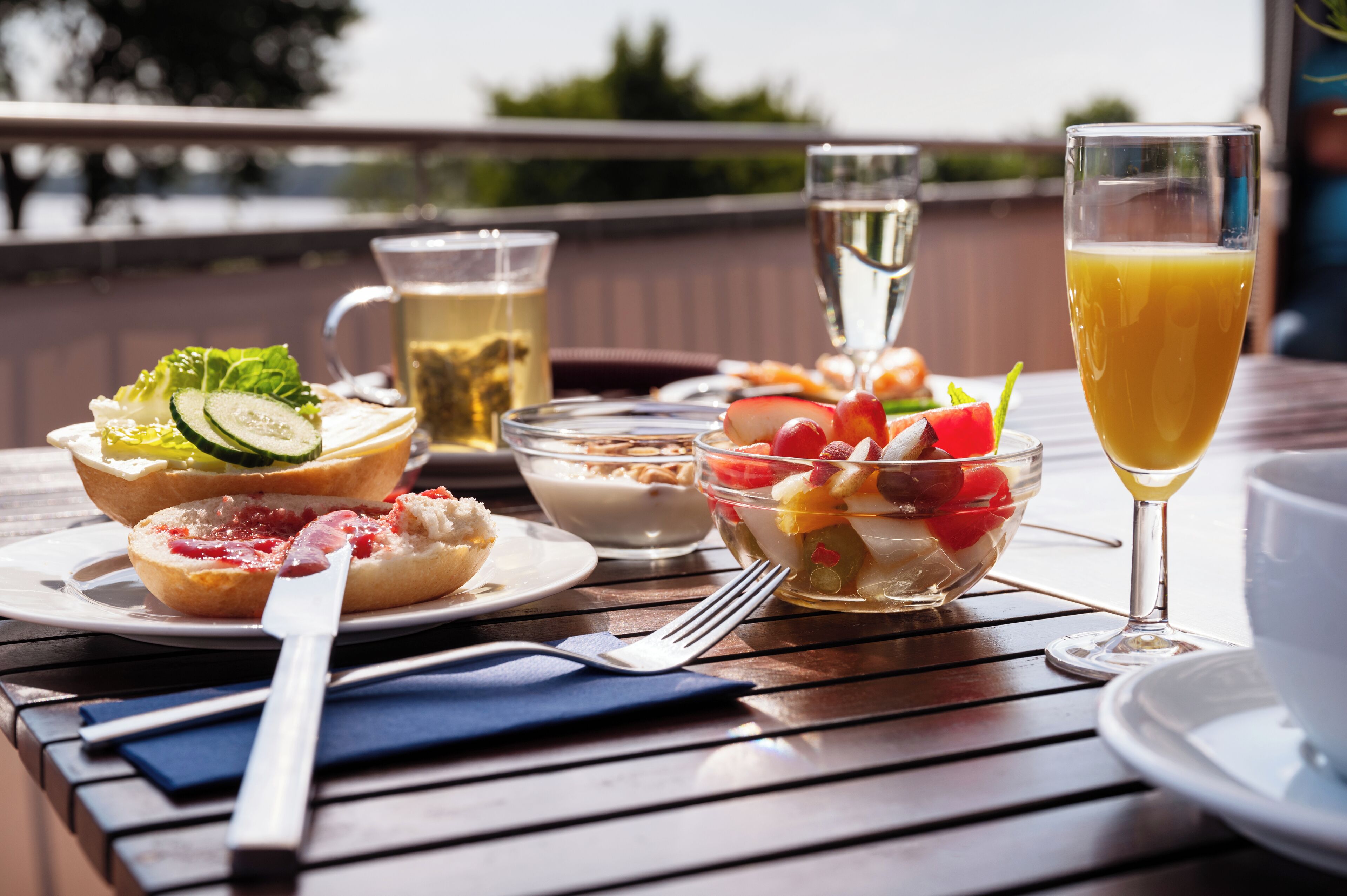 Una mesa con comida que incluye pan, ensalada y fruta, además de un vaso de jugo y una jarra de té.