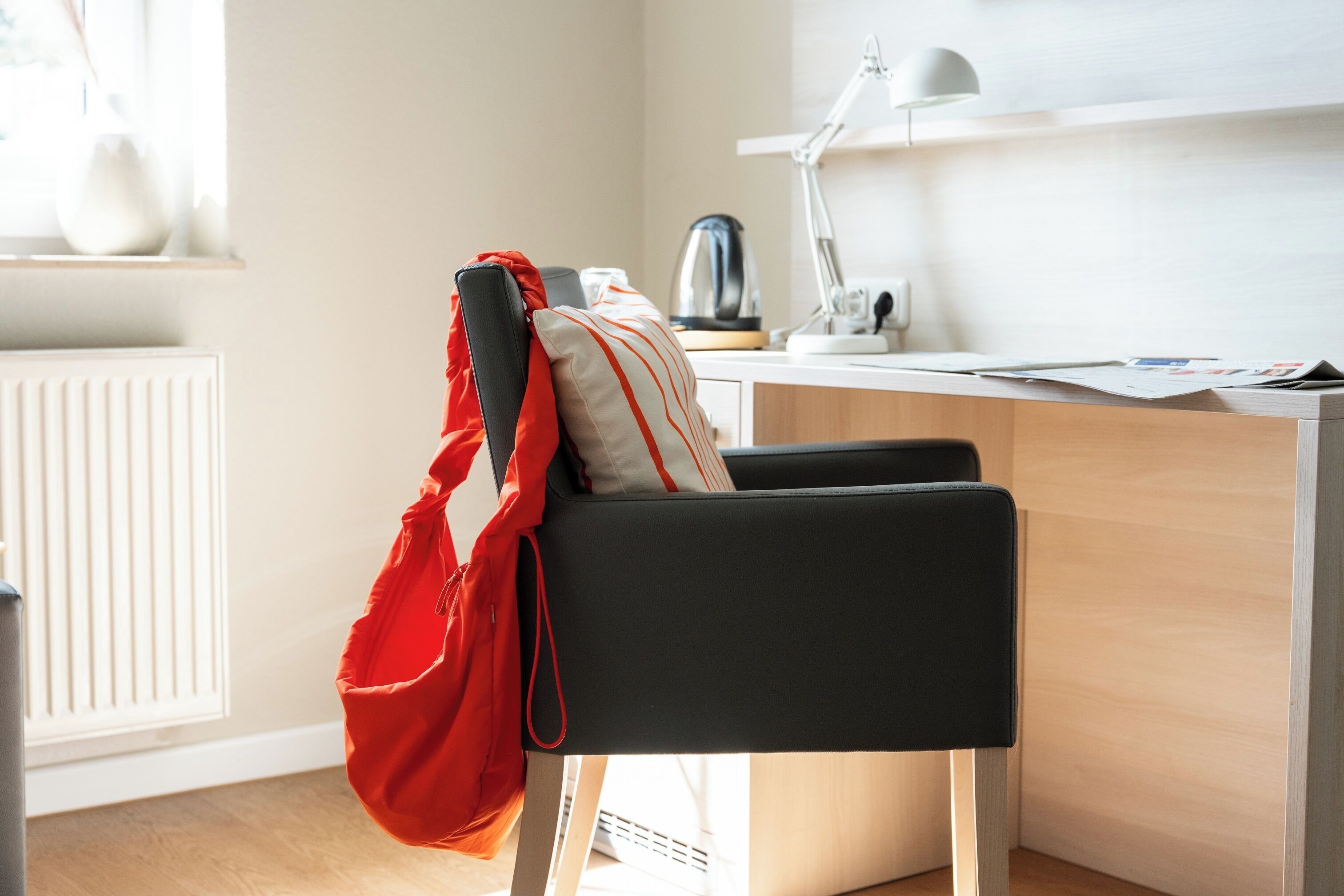 Una habitación moderna con una silla negra, un bolso rojo, un hervidor, una lámpara y un radiador.