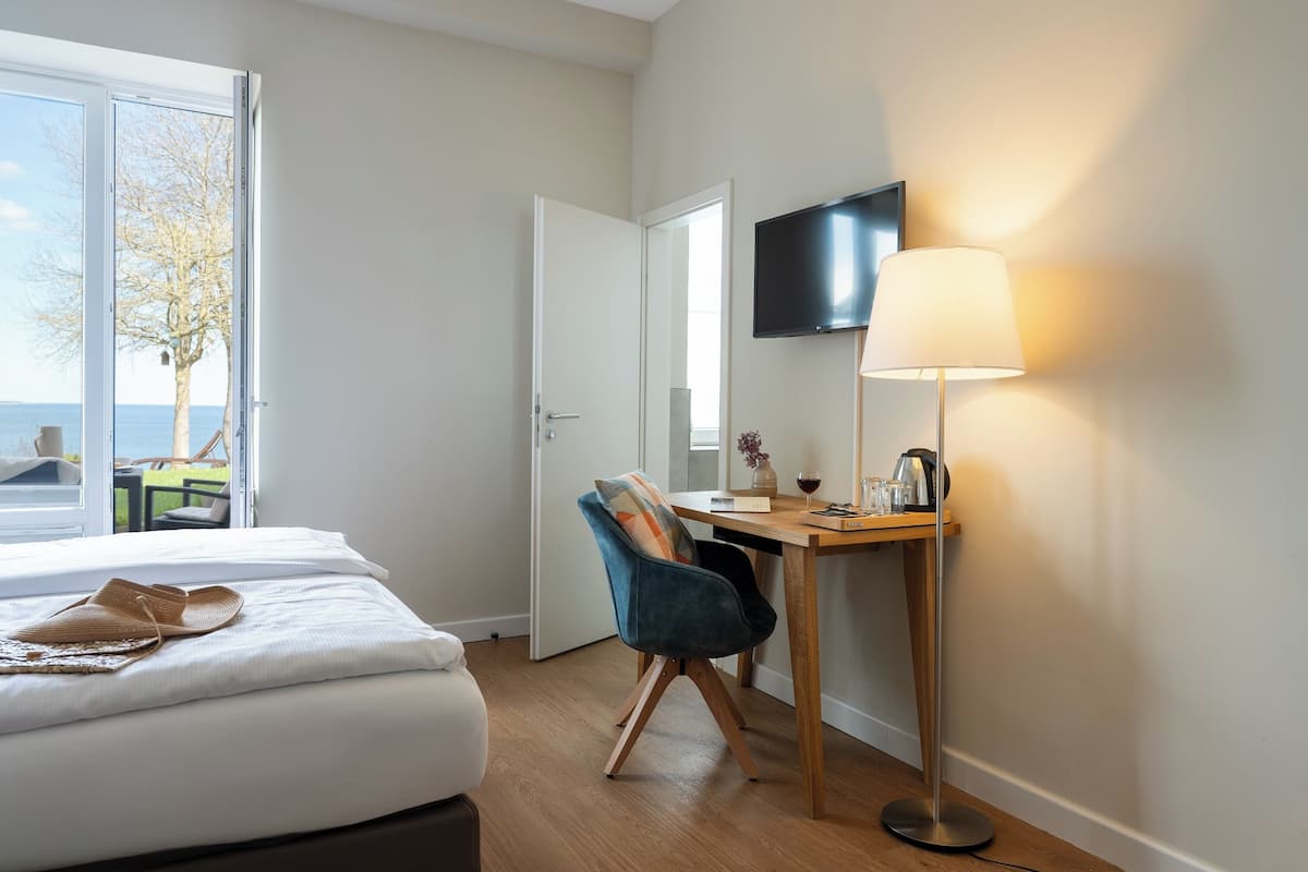 A hotel room with a bed, a desk with a chair, a TV mounted on the wall, and a window with a view of the outdoors.