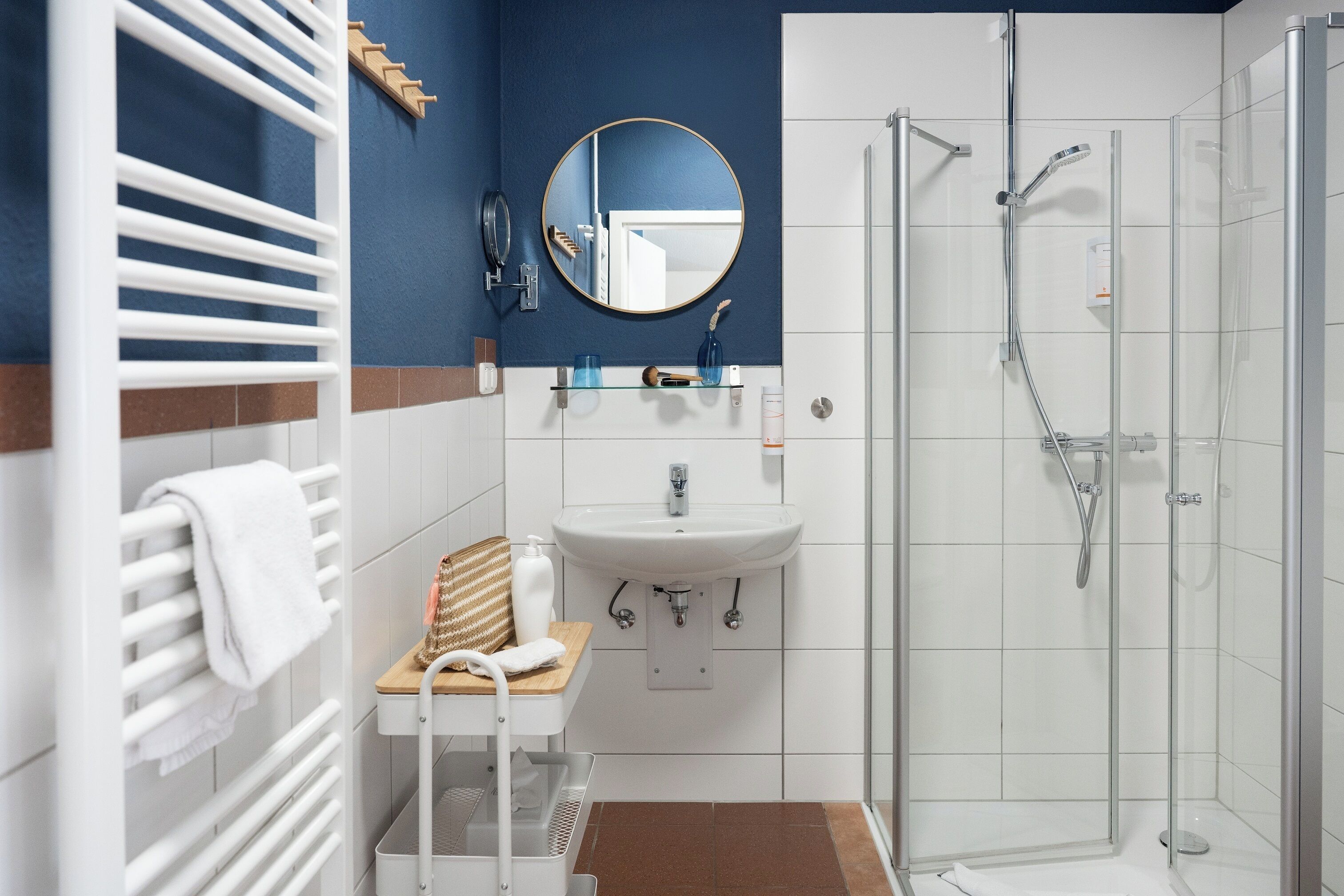 Une salle de bain moderne avec un lavabo blanc, un miroir, un porte-serviettes, une cabine de douche et un tabouret en bois.