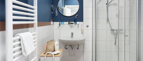 Une salle de bain moderne avec un lavabo blanc, un miroir, un porte-serviettes, une cabine de douche et un tabouret en bois.