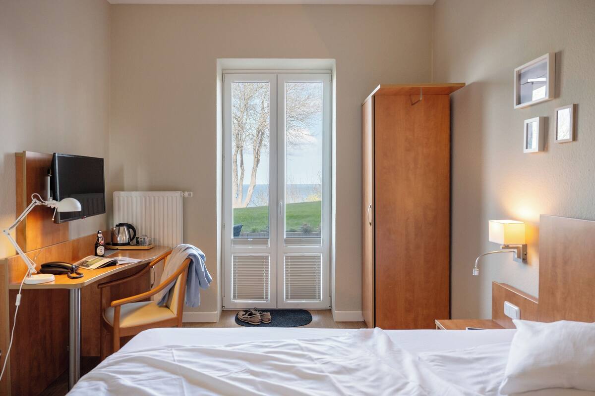 A hotel room with a bed, desk, chair, television, and a door leading to a balcony.