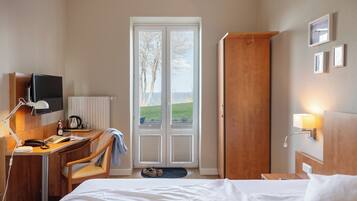 Habitación de hotel con cama, escritorio, silla, televisor y puerta que da a un balcón.