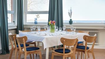 Mesa de comedor preparada para seis personas con sillas, un jarrón de flores y vista al mar.