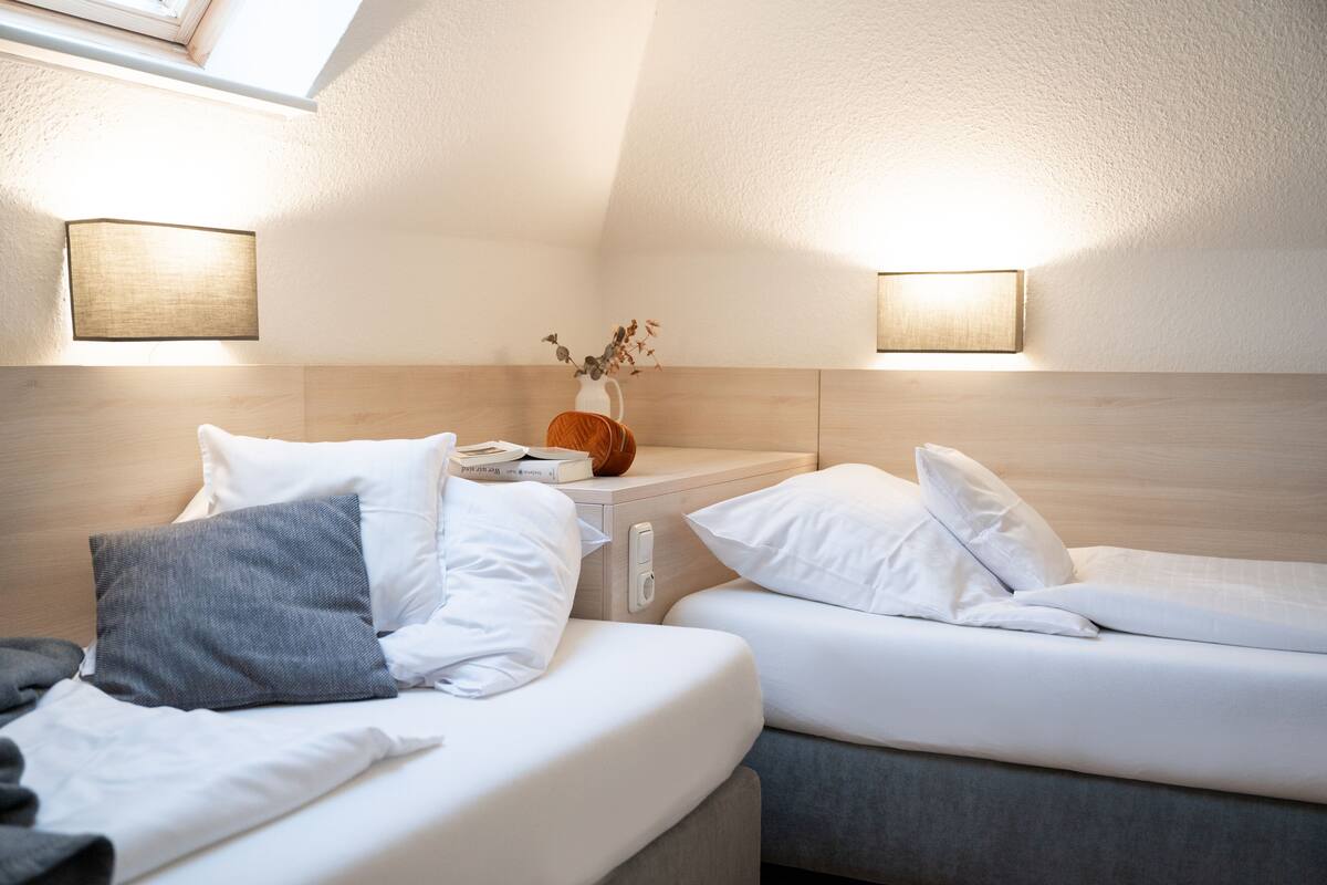 A bedroom with two beds, a bedside table with a vase, and wall-mounted lamps.