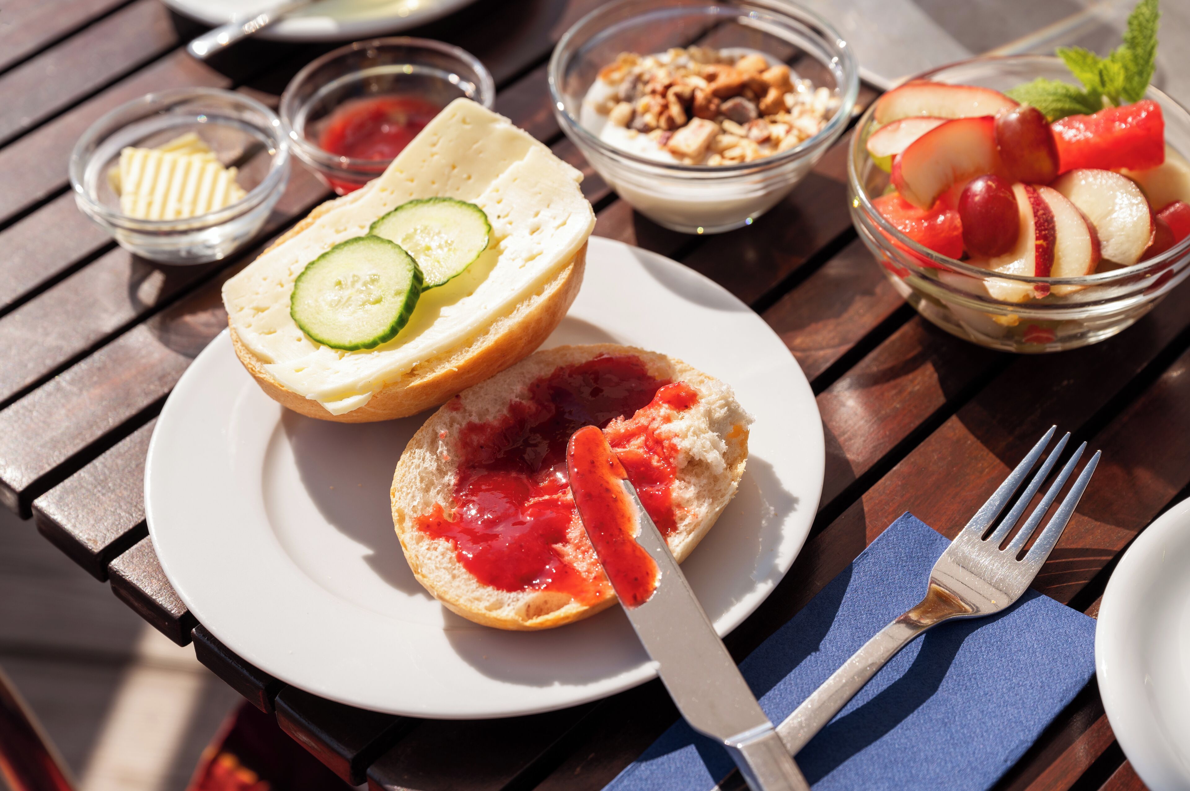 A table with a plate of sandwiches, a bowl of fruit, and a small dish of jam.