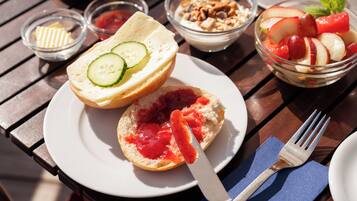 A table with a plate of sandwiches, a bowl of fruit, and a small dish of jam.