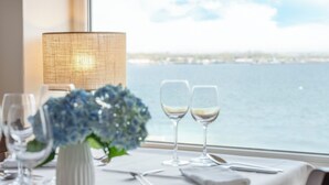 A table set with wine glasses and a vase of flowers, a lamp, and a view of the water. - Alte Fischereischule (Eckernfoerde)