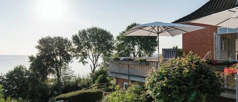 A seaside property with a balcony overlooking the sea, a large umbrella, and a brick building.