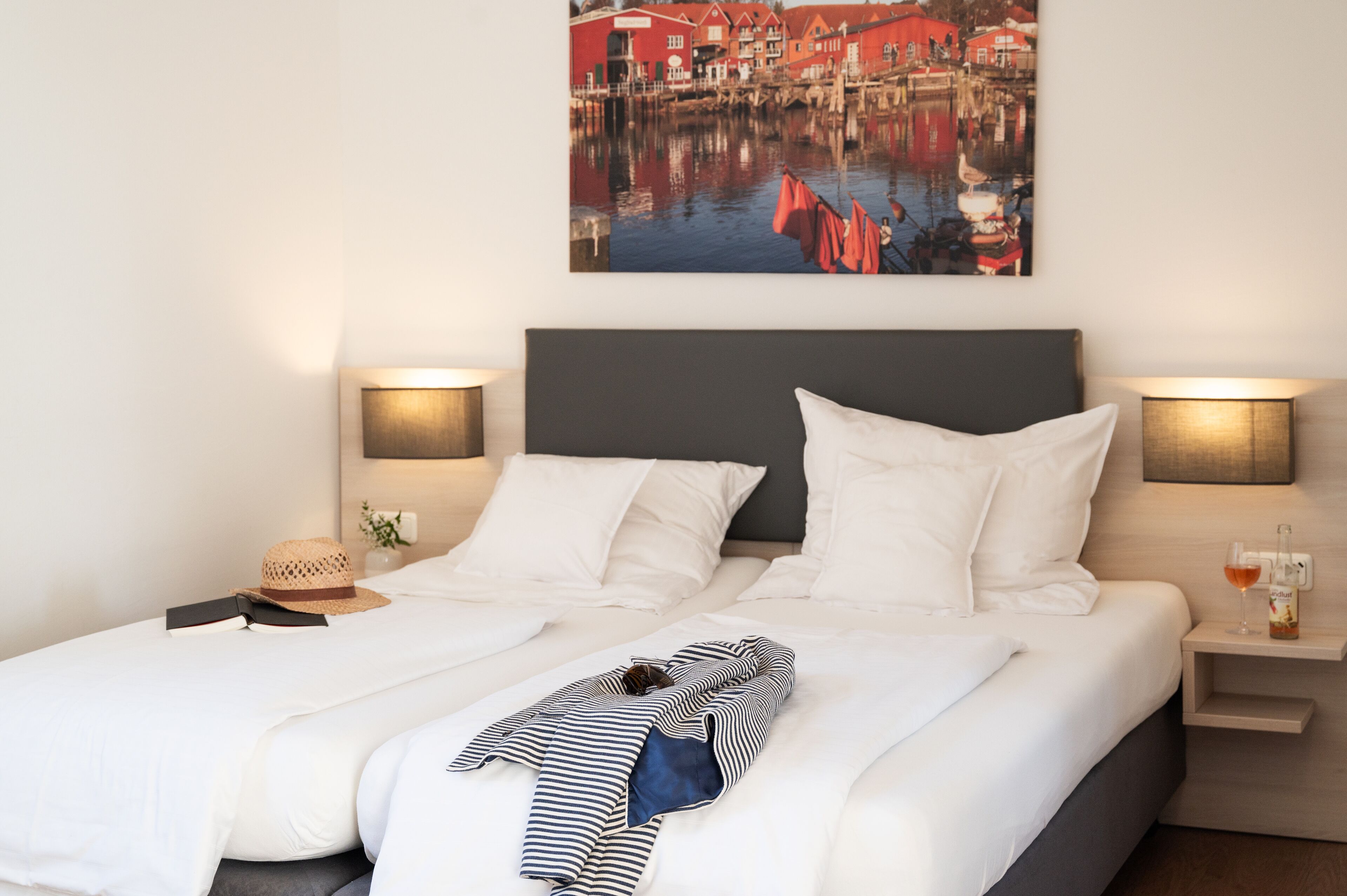 Une chambre d’hôtel avec un lit soigneusement fait, un tableau représentant un bâtiment rouge accroché au mur et deux lampes de chevet.