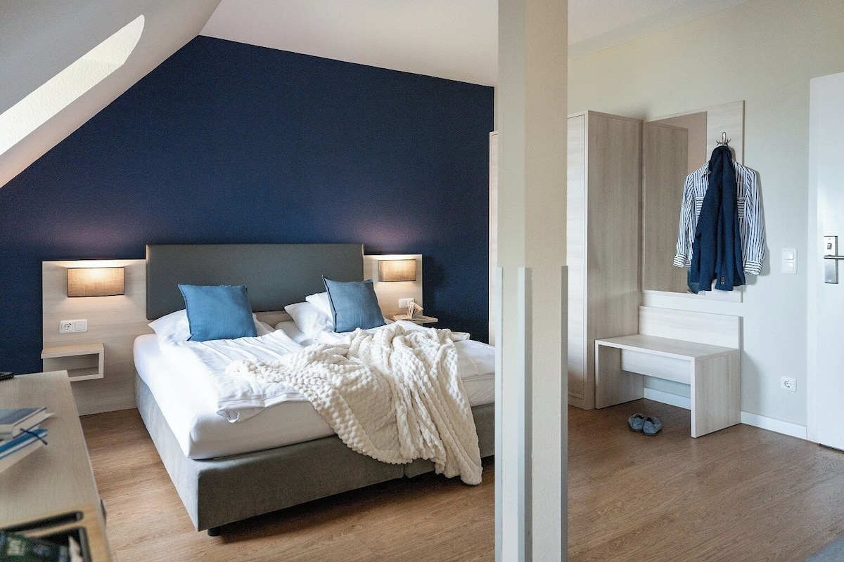 A modern bedroom with a bed, bedside tables, a desk, and a hanging coat rack.