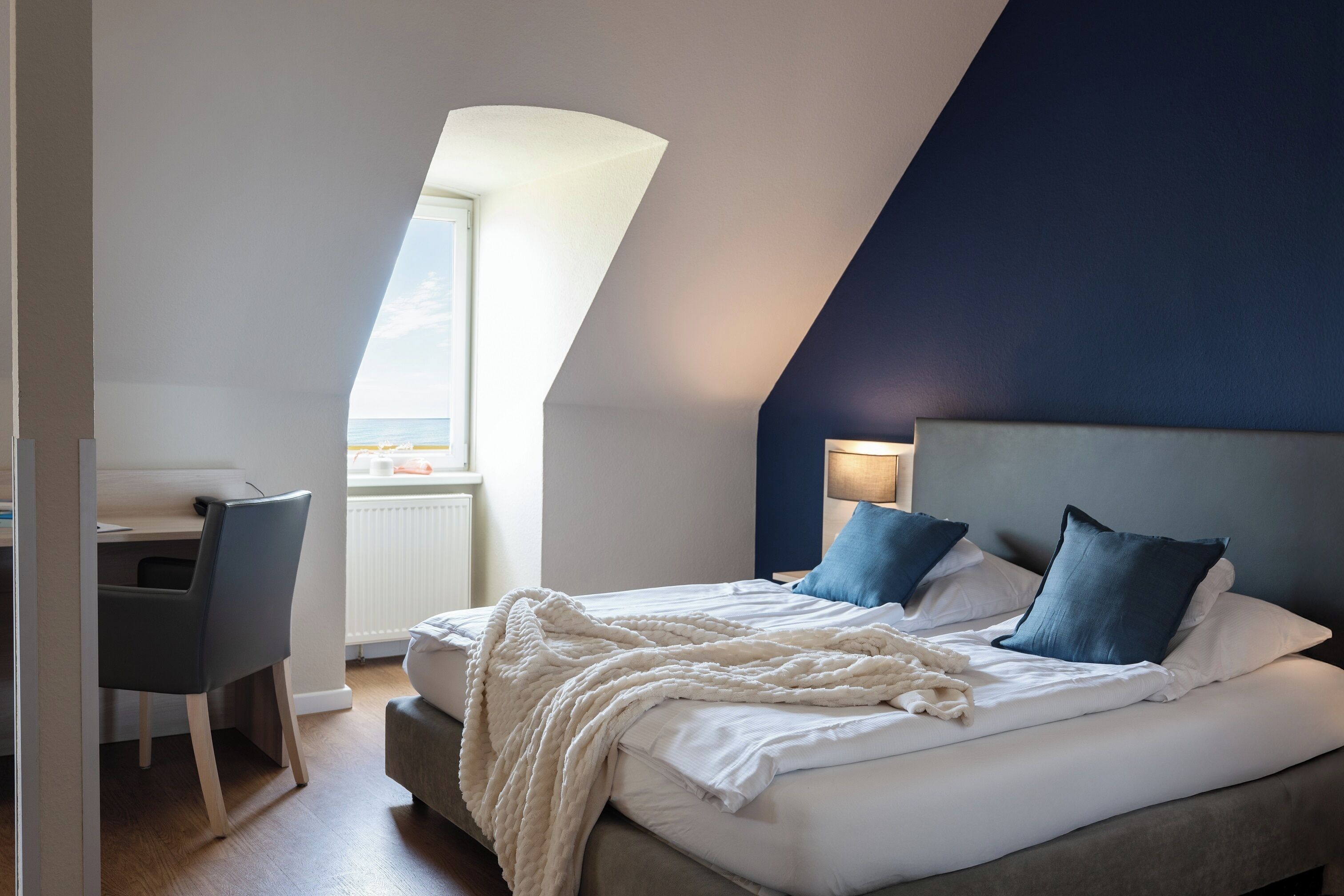 Une chambre à coucher comprenant un lit, un bureau et une chaise, une fenêtre avec vue et un plafond en pente.