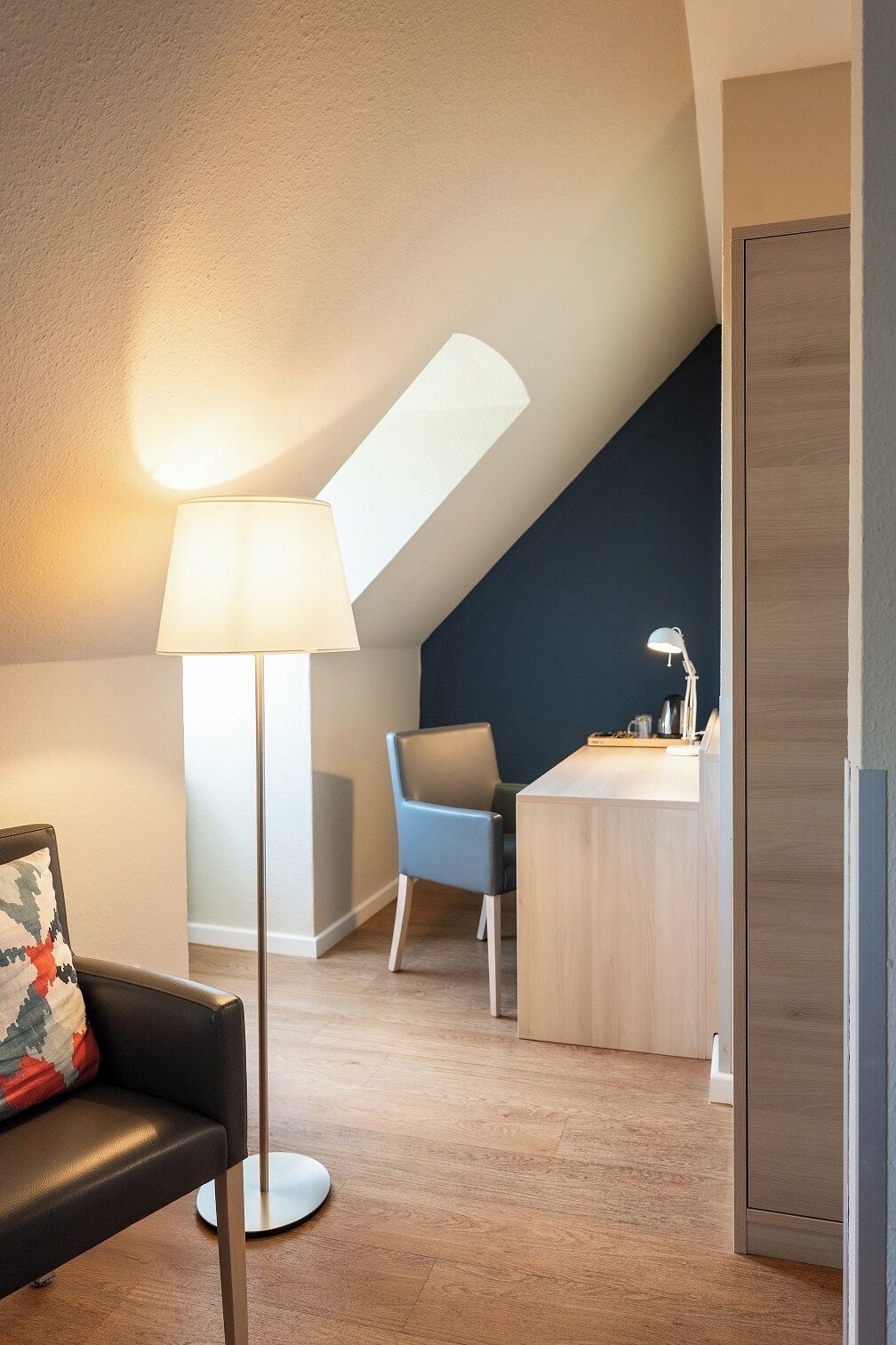 A modern room with a desk, a chair, a lamp, and a sofa.
