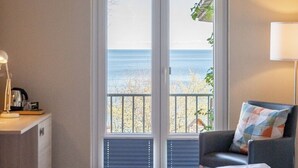 A hotel room with a bed, a desk with a lamp, a chair, and a view of the sea through a glass door. - Alte Fischereischule (Eckernfoerde)