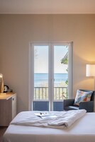 Ein Hotelzimmer mit Bett, Schreibtisch mit Lampe, Stuhl und Blick aufs Meer durch eine Glastür.
