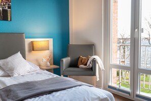 Relax in a stylish room with a comfortable bed, armchair, and large window offering a view of the outdoors.