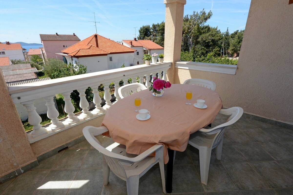 A balcony with a table set for two, featuring a pink tablecloth, white chairs, and a vase with flowers.