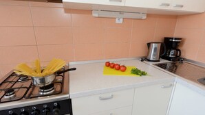 A kitchen with a gas stove, a pot of spaghetti, a cutting board with tomatoes and parsley, and a coffee maker. - Apartments Padrenostro (Zadar)