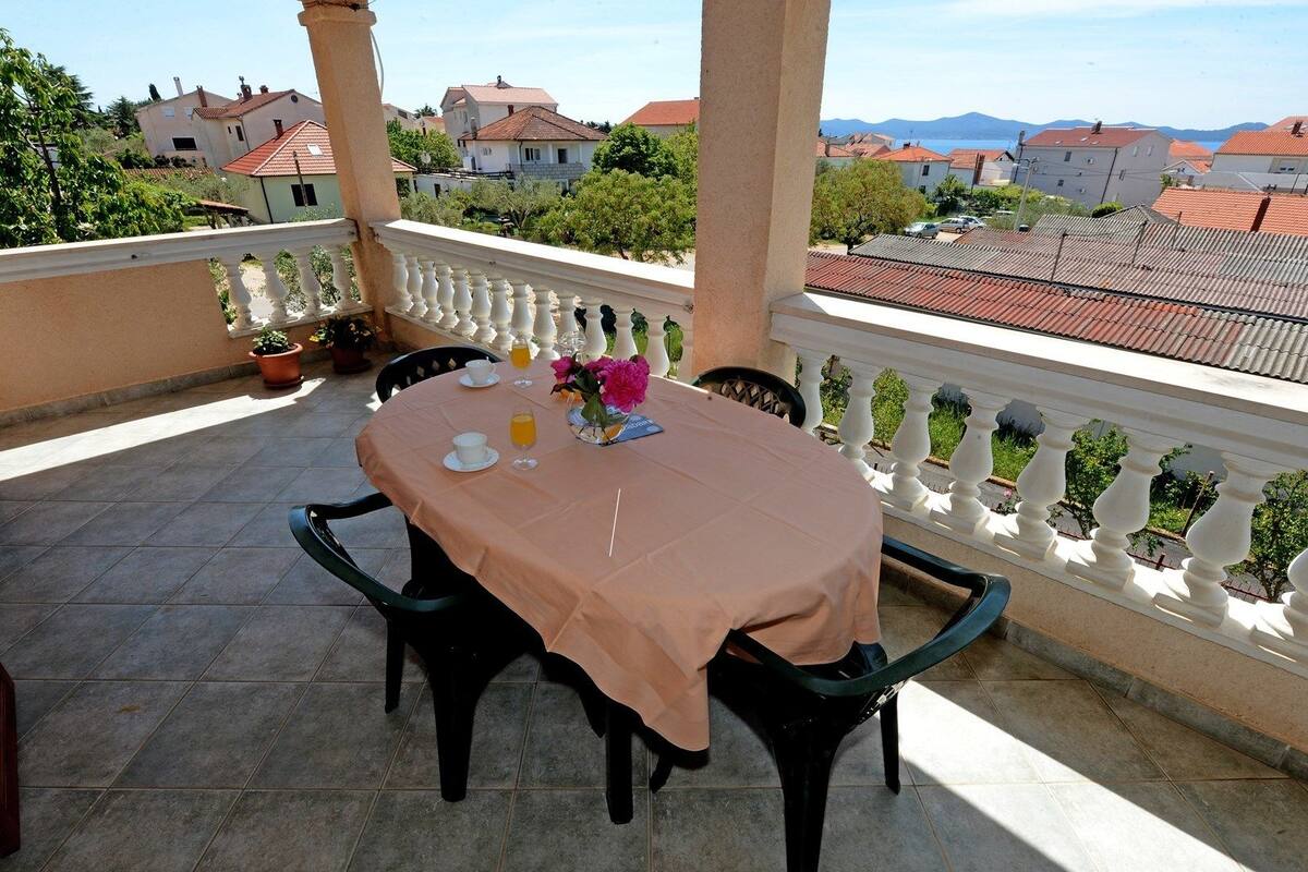 A balcony with a table set for two, featuring a tablecloth, chairs, and a vase of flowers.