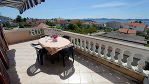A terrace with a table set for two, a balustrade, and a view of a coastal town. - Apartments Padrenostro (Zadar)