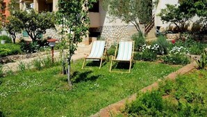 A two-story building with a balcony, surrounded by a garden with grass and small trees. - Apartments Padrenostro (Zadar)