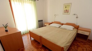 A bedroom with a wooden bed, bedside tables, a radiator, a window with curtains, and a small plant on a side table. - Apartments Padrenostro (Zadar)