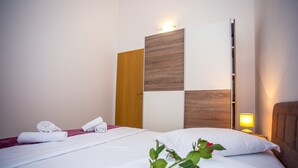 Ein Hotelzimmer mit einem Bett, einem hölzernen Kopfteil, einem Nachttisch mit Lampe und einem an der Wand befestigten Regal.