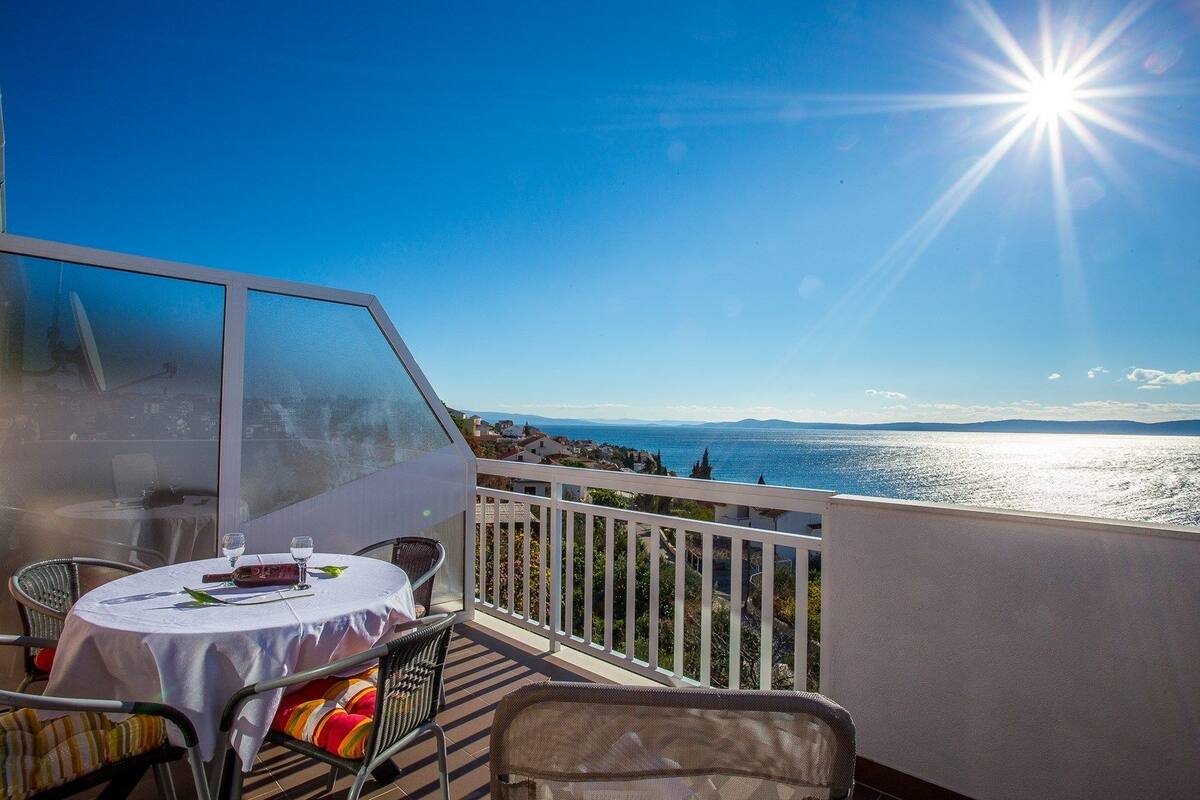 A balcony with a table set for two, overlooking a coastal view.