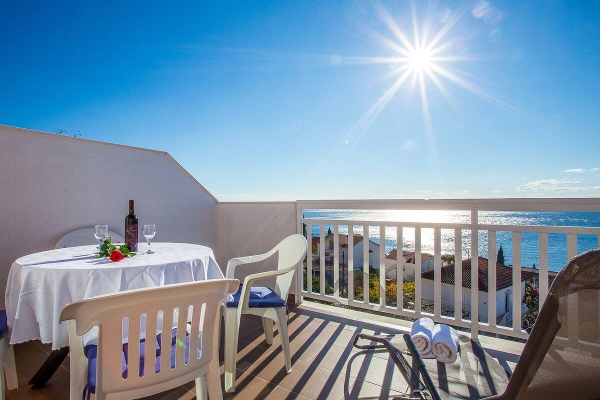 A balcony with a table set for two, a bottle of wine, and a glass.