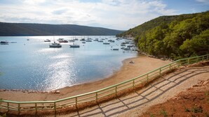 A coastal area with boats on the water, a sandy beach, and a green railing. - Villa Gelci (Rasa)