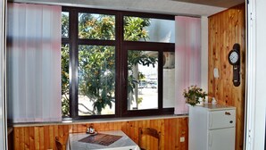 Une petite pièce avec une table et des chaises, une fenêtre avec des rideaux, un réfrigérateur et une horloge au mur.