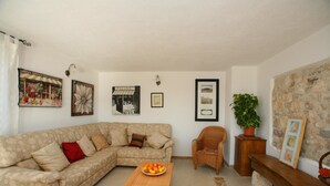 Una sala de estar con un sofá, una mesa de centro de madera con fruta, una silla de mimbre y una pared de piedra.