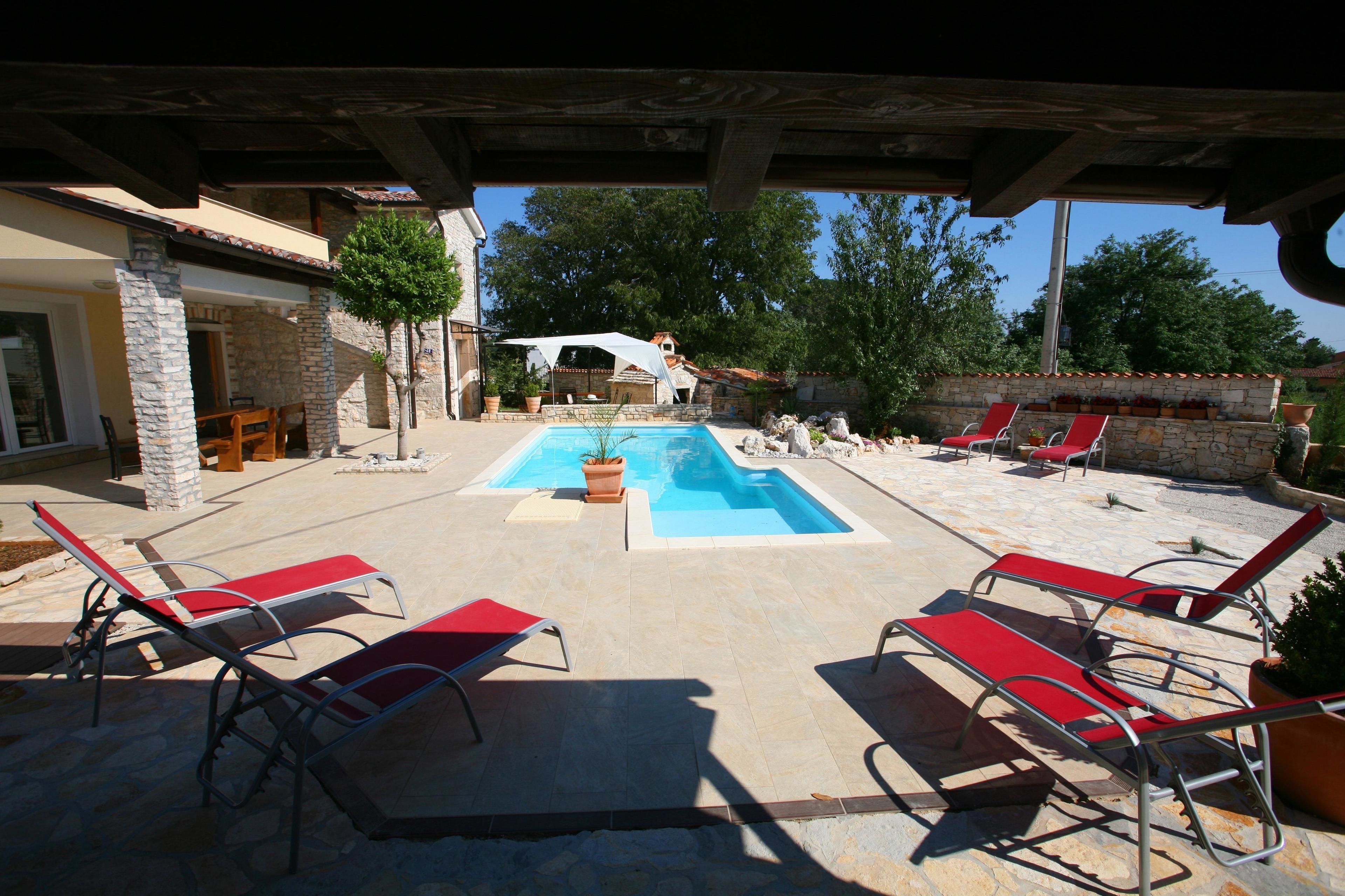 A pool area with lounge chairs, a covered seating area, and stone walls.
