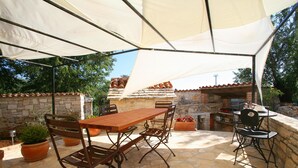 Un patio al aire libre con una mesa y sillas de piedra, rodeado de plantas en macetas y un muro de piedra.