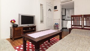 A compact living space with a television, a wooden table, a sofa, and a kitchen area visible through an open door.