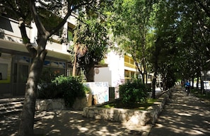 A tree-lined pathway with stone planters and a building with signage. - Family Apartment Teo (Split)