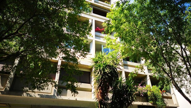 En byggnad med flera våningar och balkonger, omgiven av frodig grönska.