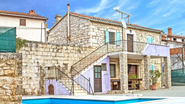 Un edificio in pietra con piscina, una scala e un balcone.